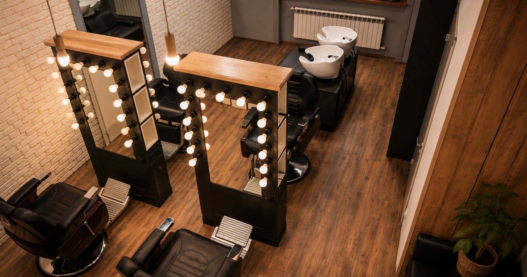 Overhead view of a salon floor with styling chairs, lit vanity mirrors, and wash stations.