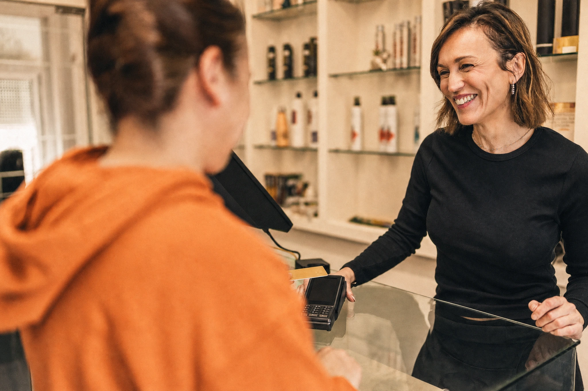 A smiling salon professional taking a client's card payment on a terminal at the front desk.